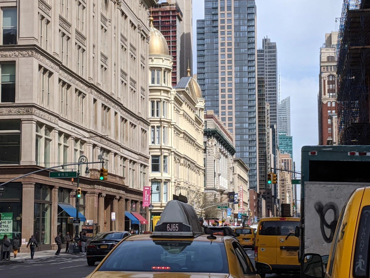 A busy city street with taxis, pedestrians, and tall buildings, including an ornate one with a golden dome.