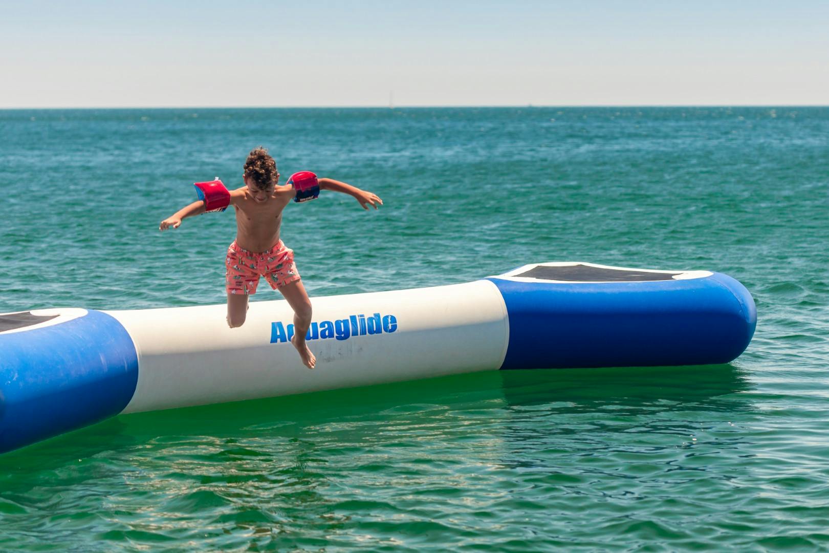 「アクアグライド」と書かれた膨脹可能な水のおもちゃから飛び降りる子ども。