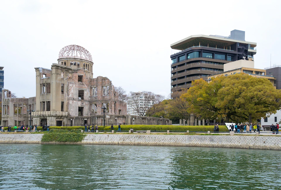 A riverside park with the Hiroshima Peace Memorial Dome and modern buildings in the background.
