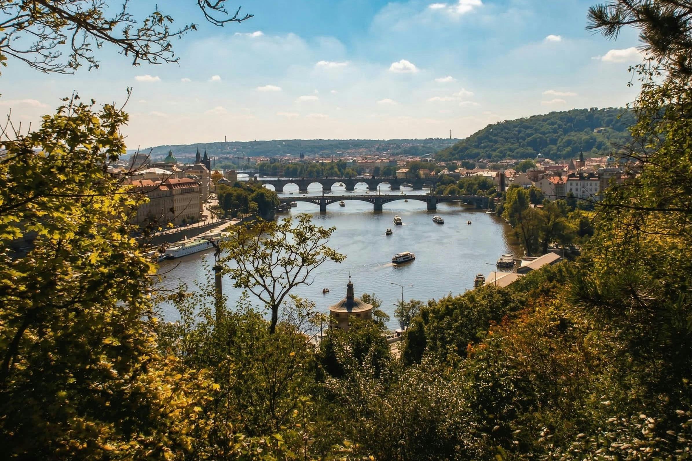 A scenic view of a river with multiple bridges, surrounded by a city and greenery under a partly cloudy sky.