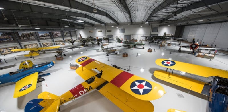 Hangar del museu d'aviació que mostra diversos avions militars, amb avions grocs i blaus amb insígnies i objectes de l'època de la guerra.