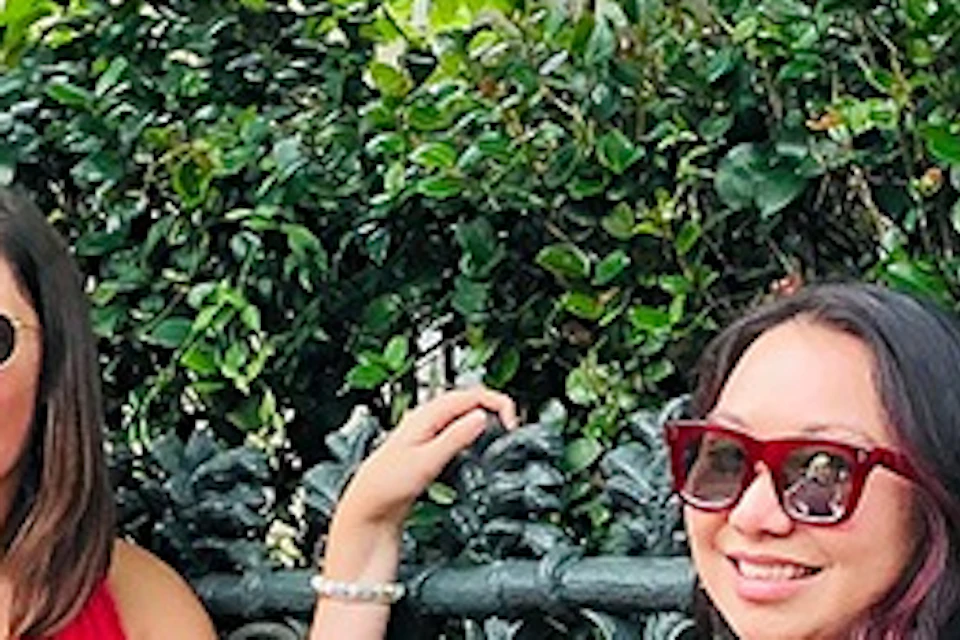 Three people posing near an ornate fence in an outdoor setting with greenery. One person leans on the fence playfully.