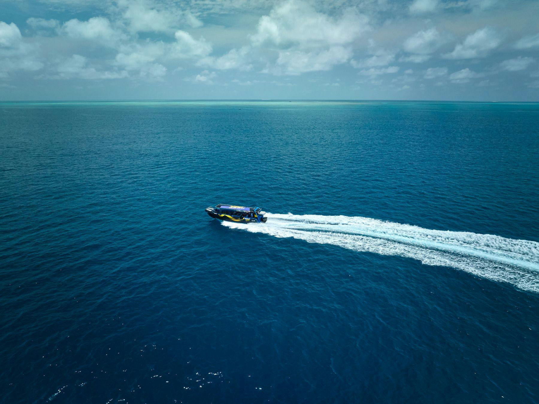 スピードボートは、部分的に曇った空の下で広大な青い海を移動するときにウェイクを作成します。