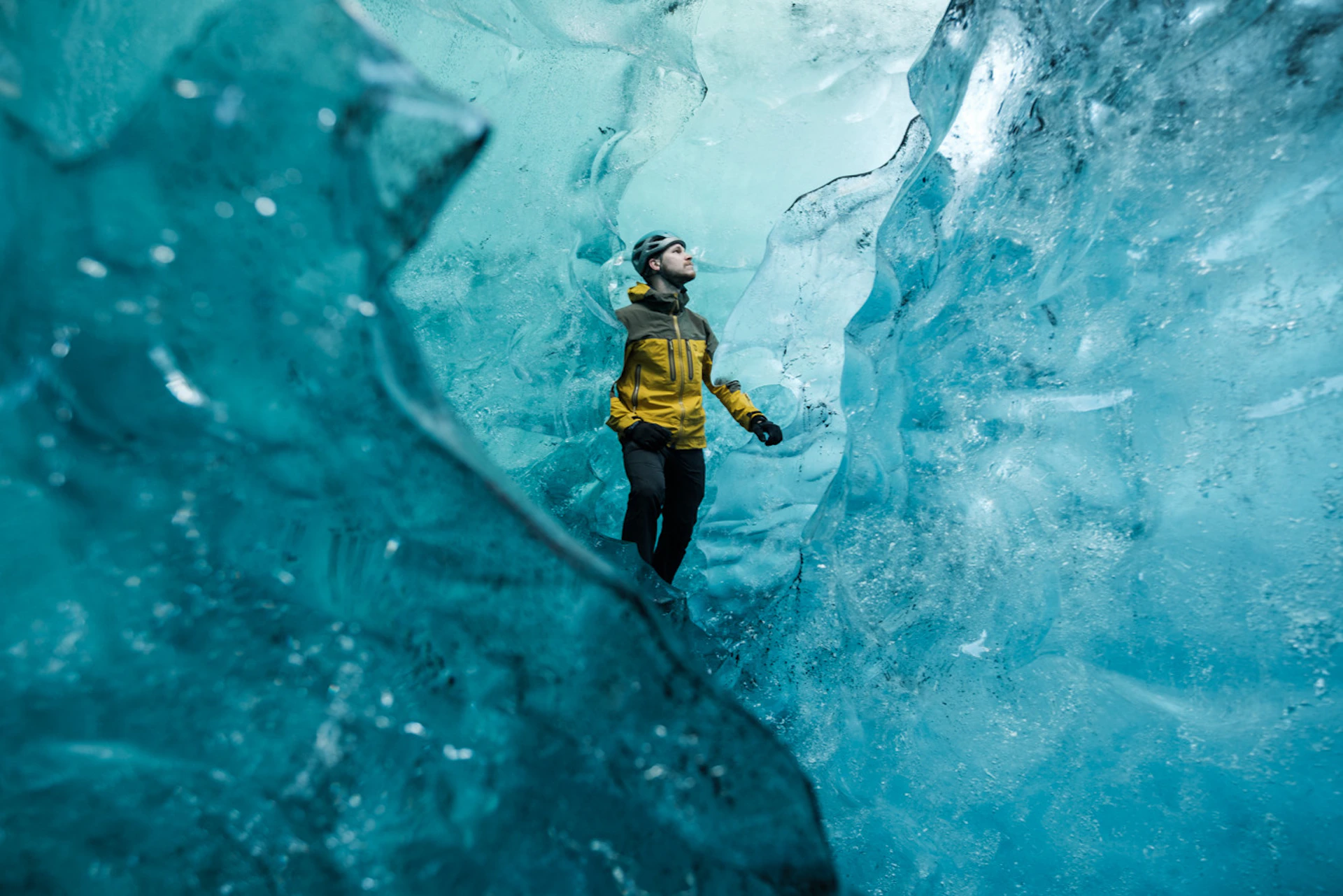 Person in a yellow jacket exploring inside a blue ice cave.