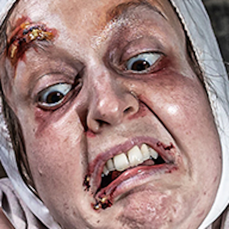 A person in historical attire with a distressed expression holds a bloody rope, over a blood-stained cloth in a dim, eerie room.