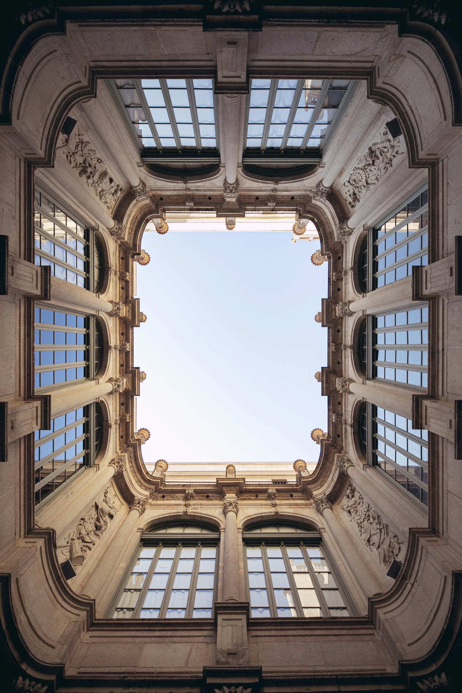Vue symétrique d'une cour rectangulaire ornée de détails et de grandes fenêtres, encadrant un ciel bleu clair.