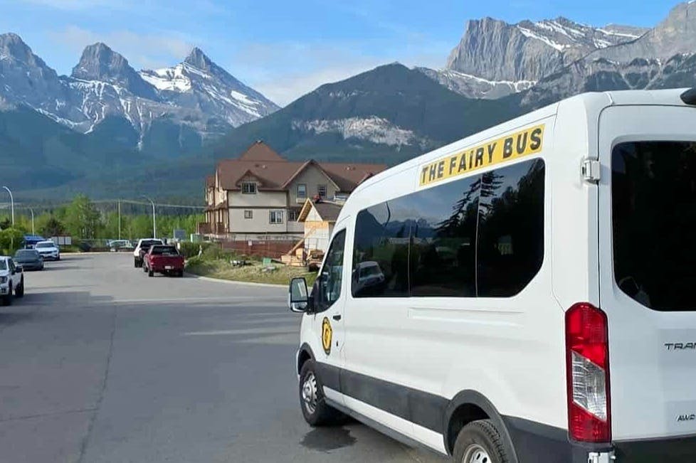 A white van labeled "The Fairy Bus" parked in a residential area with mountains in the background.