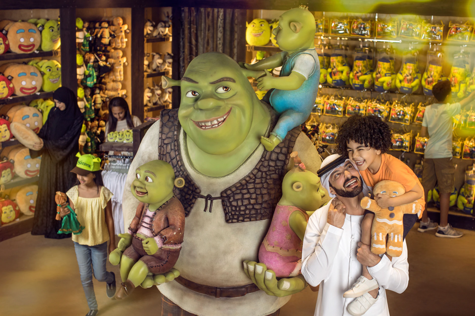 People posing with statues of Shrek and his family inside a brightly lit gift shop filled with Shrek-themed merchandise.