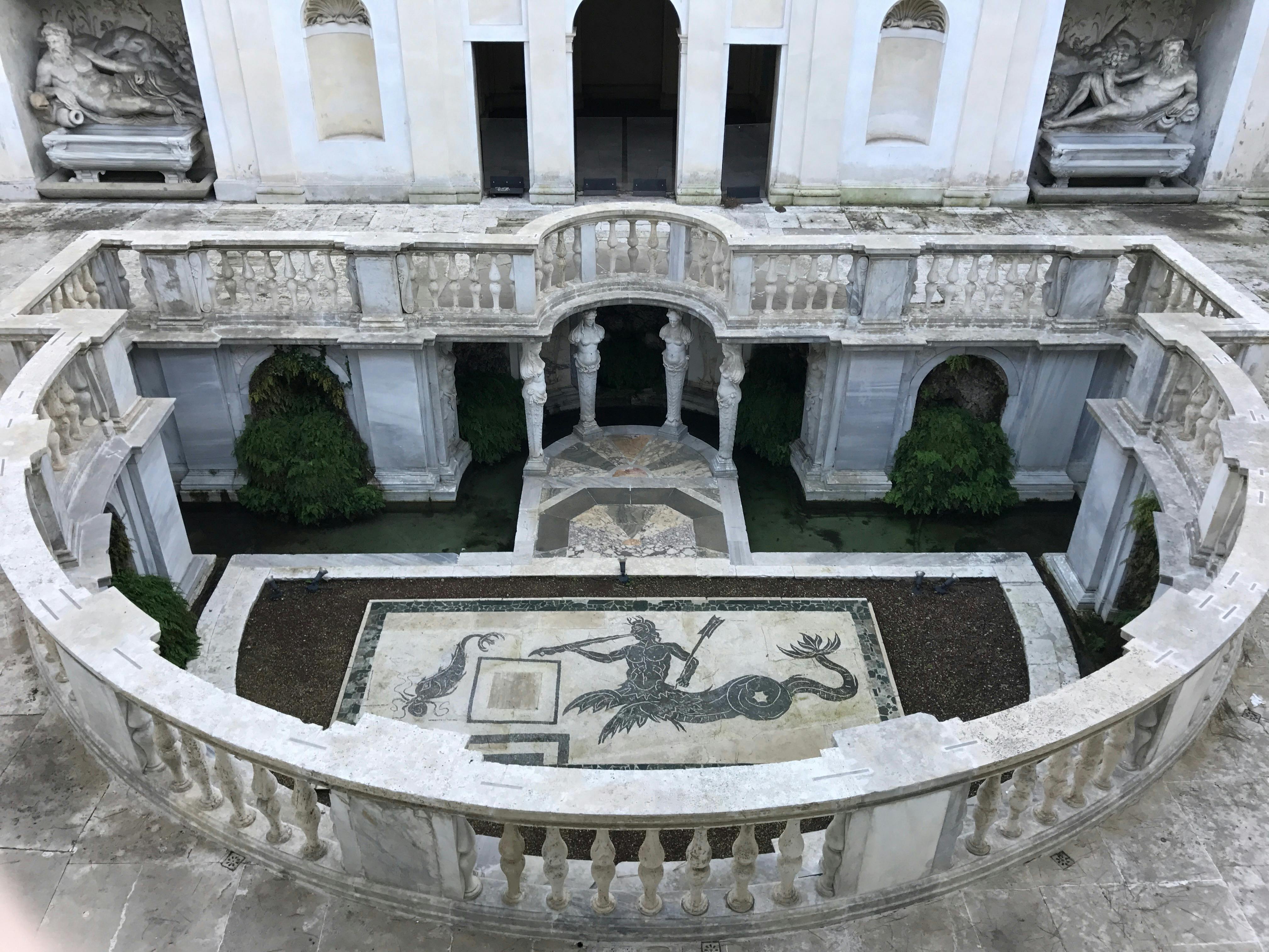 Cour ornée de balcons voûtés, de verdure et d'une mosaïque centrale représentant une sirène tenant une lance.