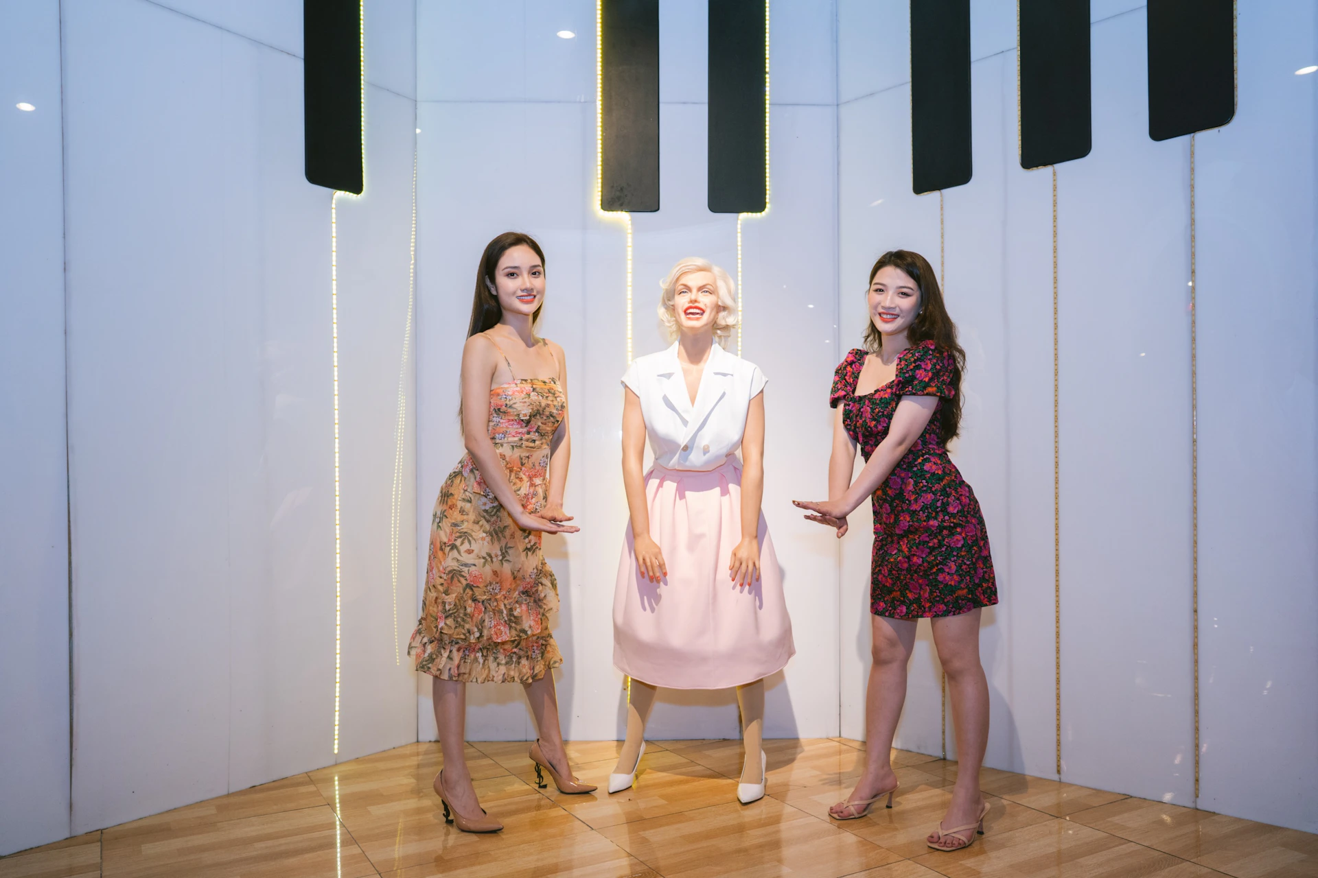 Two women pose next to a statue of a woman in a bright room with reflective flooring and wall decorations.