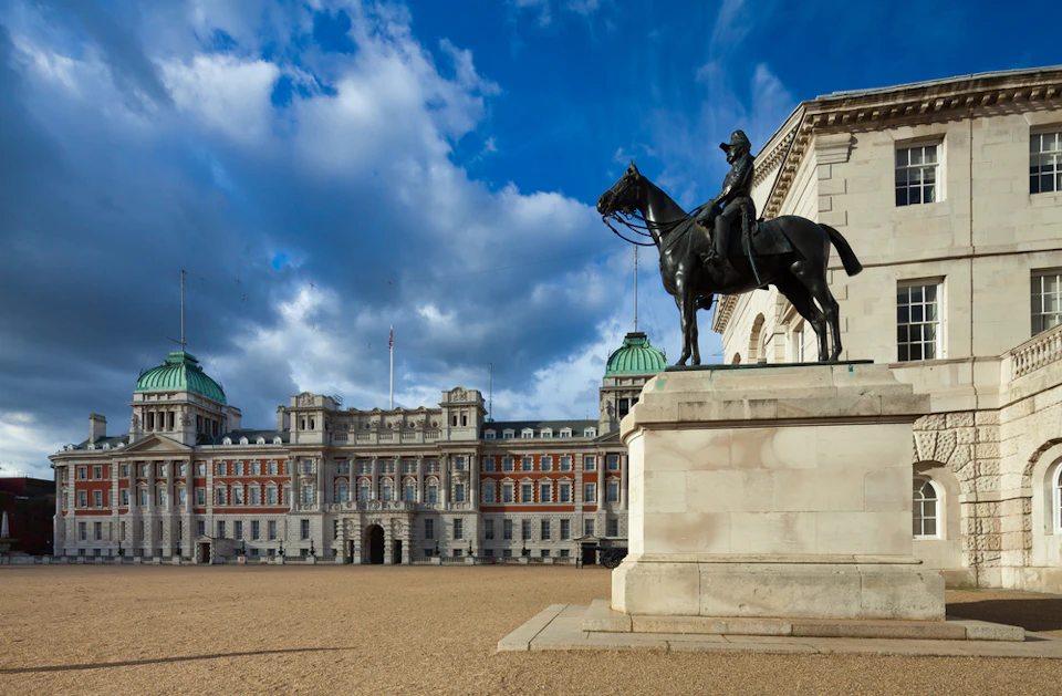 A statue of a rider on horseback in front of an ornate historic building with a large courtyard and a cloudy sky.