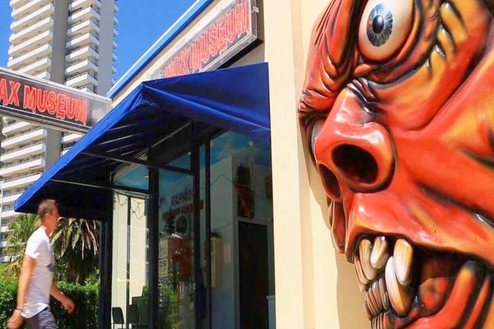 L'entrée d'un musée de cire avec une grande sculpture de visage menaçant à côté de la porte et une personne qui passe devant.