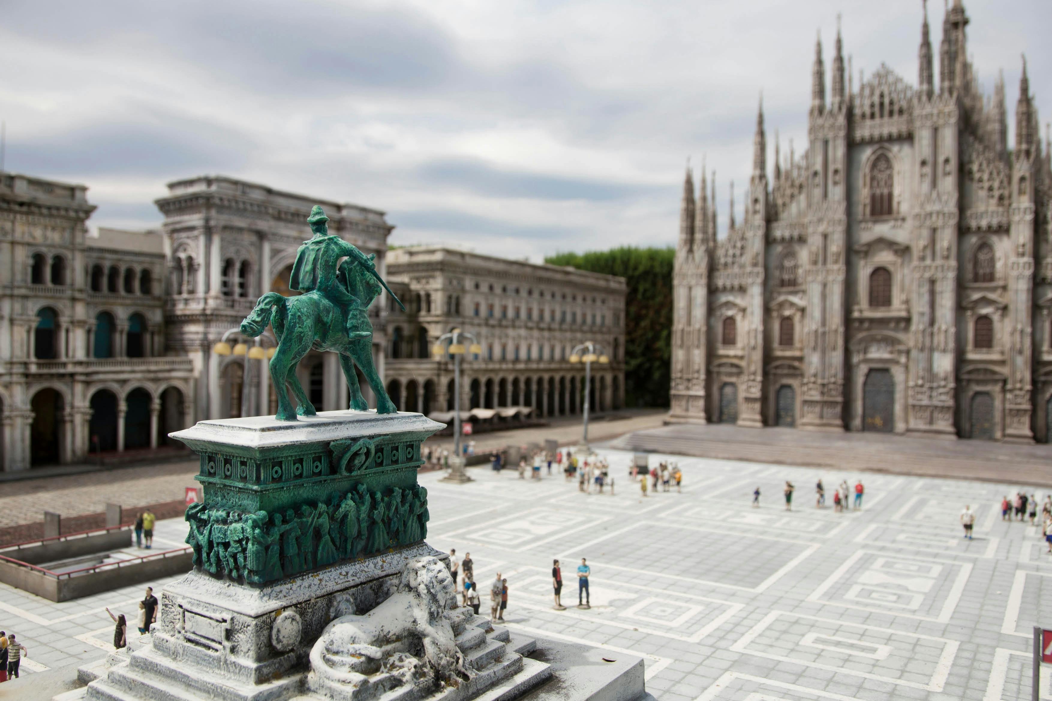Una piazza della città con una statua di cavallo e cavaliere, un'architettura dettagliata e una cattedrale sullo sfondo.