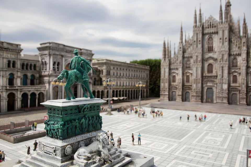 A city square with a statue of a horse and rider, detailed architecture, and a cathedral in the background.