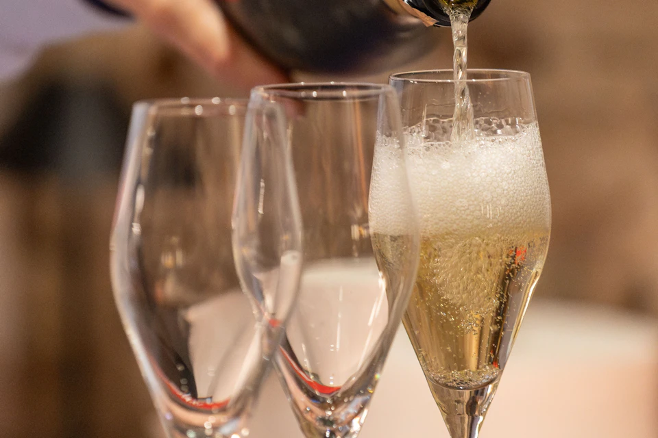 A close-up of champagne being poured into a flute glass, with two empty glasses in the background.