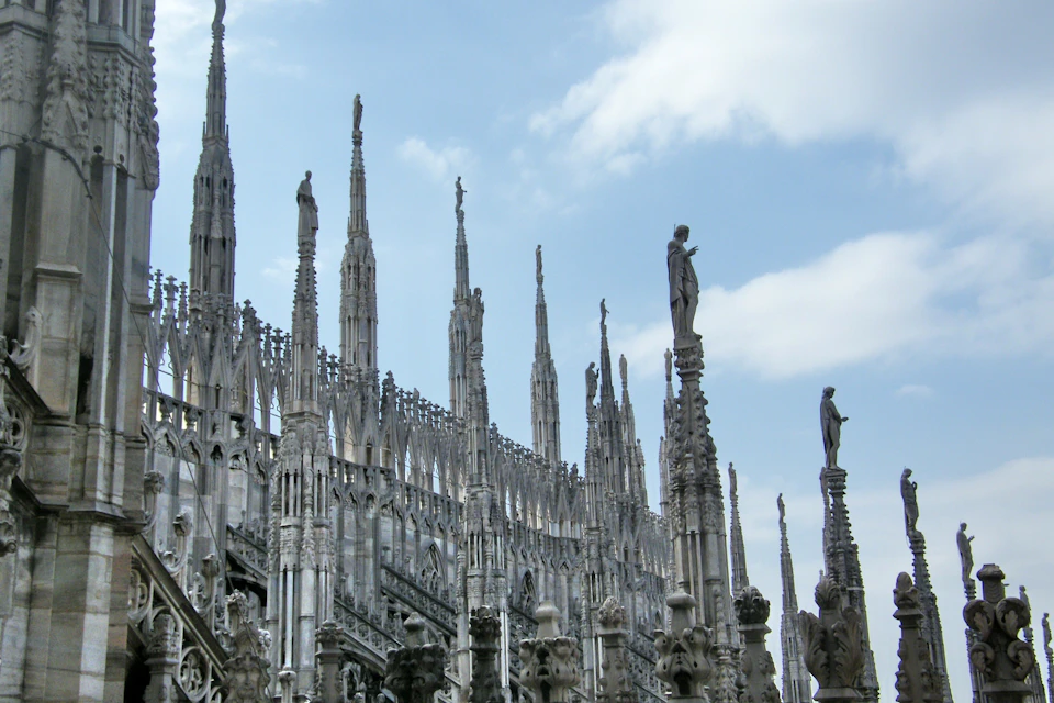 Gothic cathedral with intricate spires, pinnacles, and statues under a partly cloudy sky.