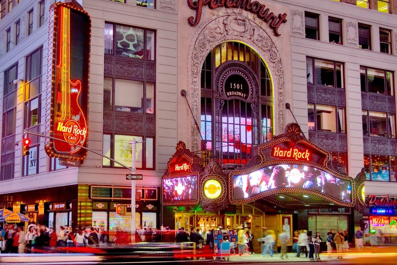 Crowded street scene in front of the Hard Rock Cafe and Paramount building at 1501 Broadway, with neon signs and busy pedestrian traffic.
