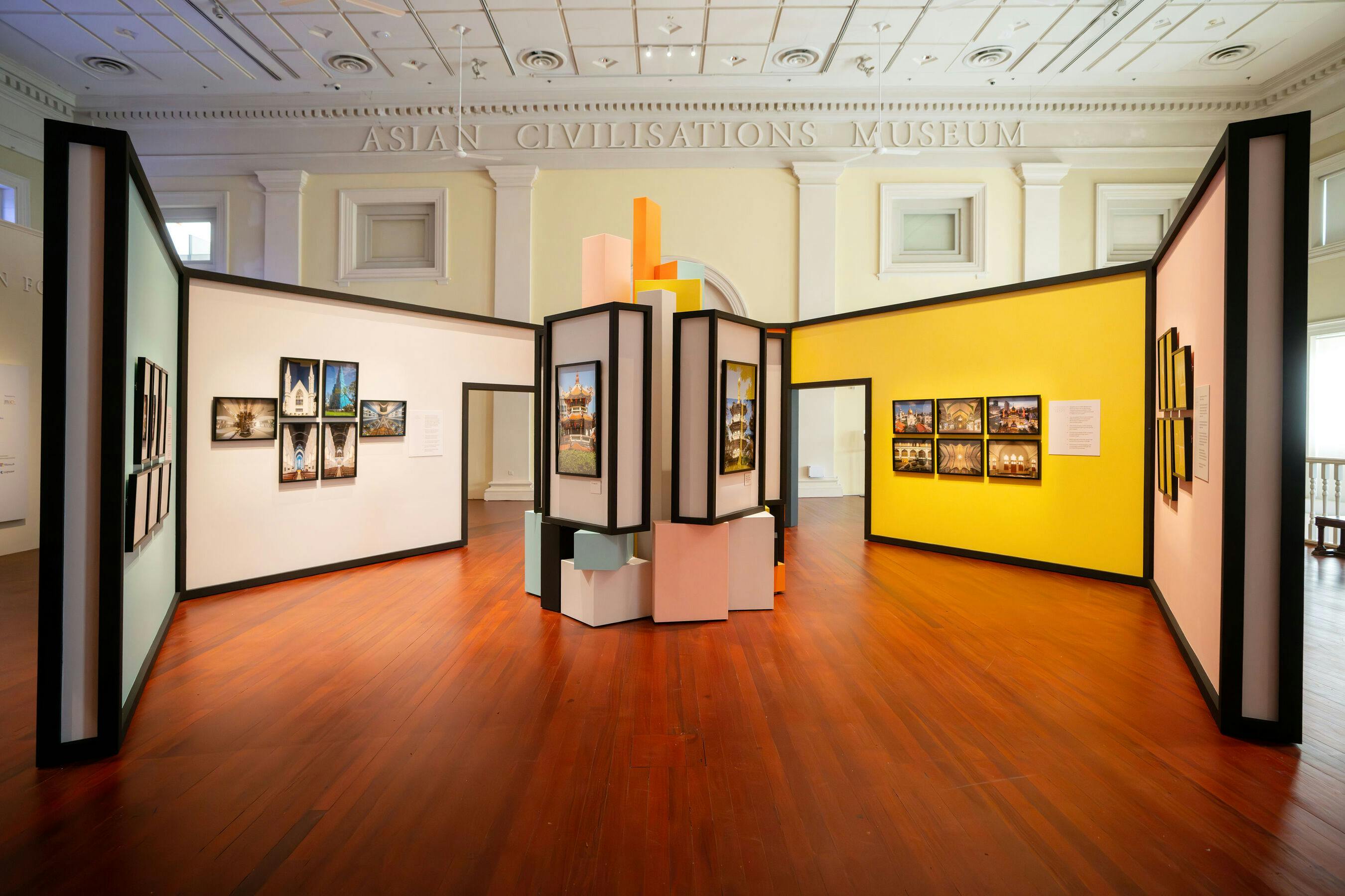 An exhibit room in the Asian Civilisations Museum featuring colorful partitions and framed art displayed on walls and panels.