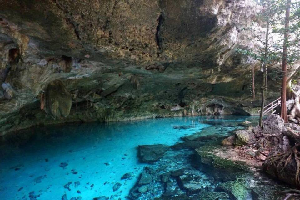 Subterranean pool with clear turquoise water and rocky cave ceiling, with rock formations above and around the water.
