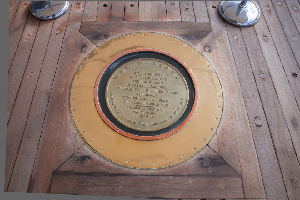 Brass plaque on a wooden deck marking the spot of Japan's WWII surrender on the USS Missouri, with some text visible on it.