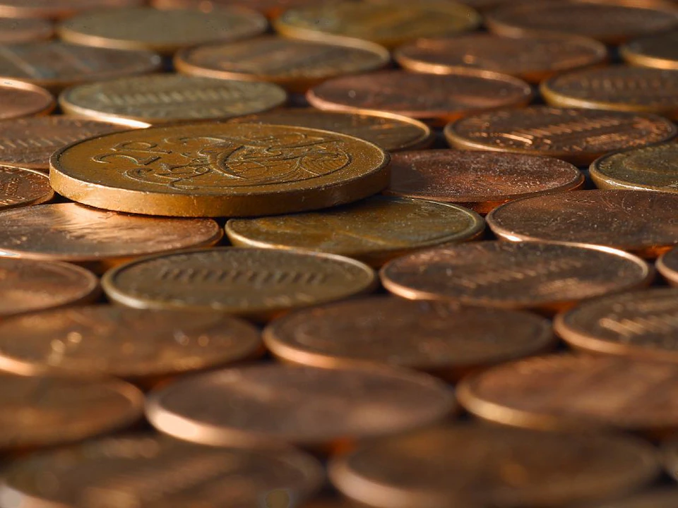 Close-up of a pile of various coins, predominantly copper-colored, with one larger coin prominently placed on top.