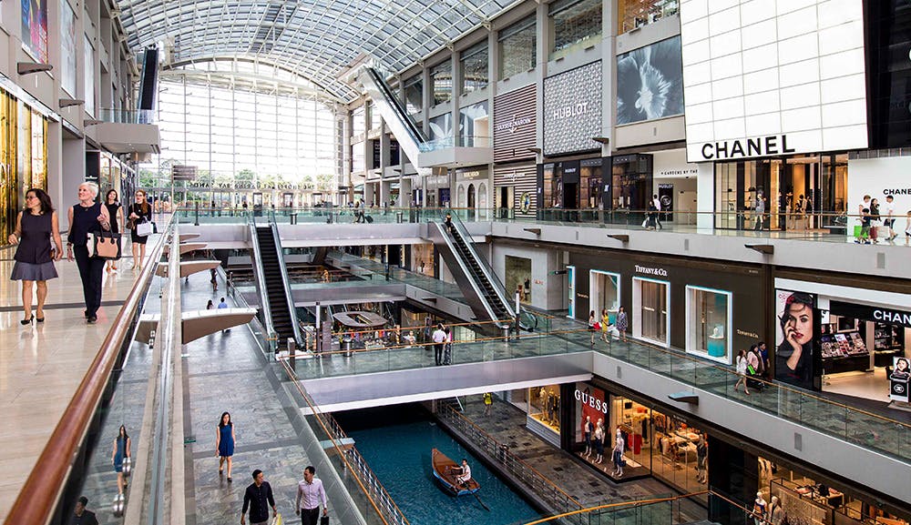 Εμπορικό κέντρο τριών επιπέδων με καταστήματα όπως το Hublot, το Chanel και το Guess. Οι αγοραστές περπατούν και μια βάρκα βρίσκεται στο εσωτερικό κανάλι.