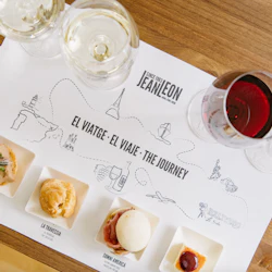 Fyra olika rätter tillsammans med två glas vitt vin och två glas rött vin på en bordstablett med titeln "Resan".