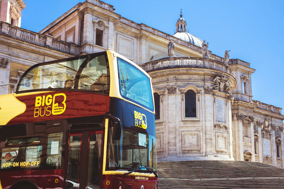 A red double-decker tour bus in front of a historic building with columns and a dome under a clear blue sky.