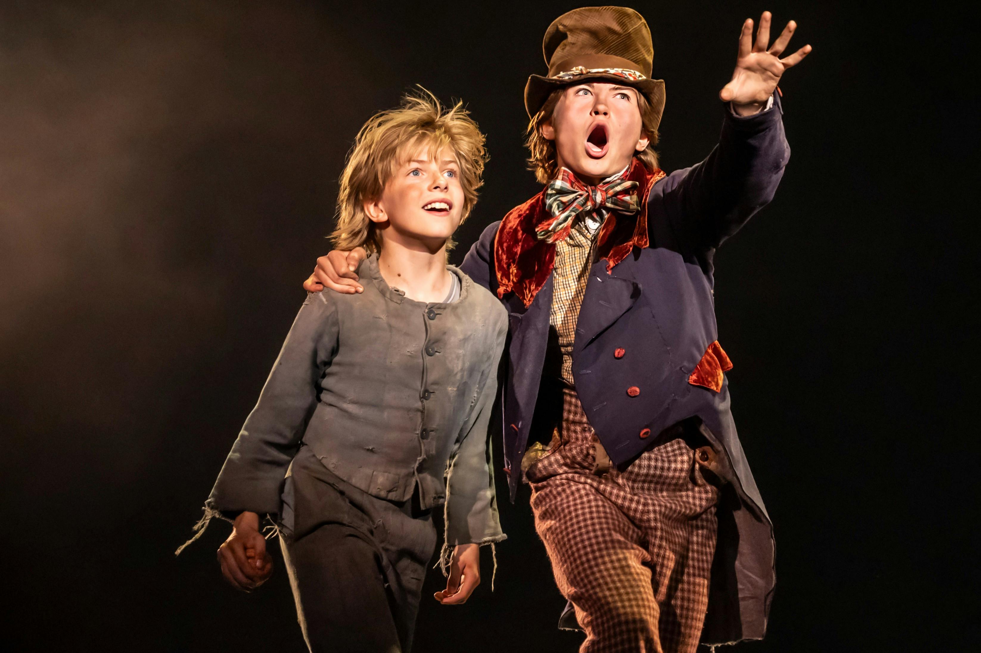 Dos nois amb roba andrajosa; un amb corbatí i barret, amb el braç al voltant de l'altre, tots dos mirant amb il·lusió cap al davant.