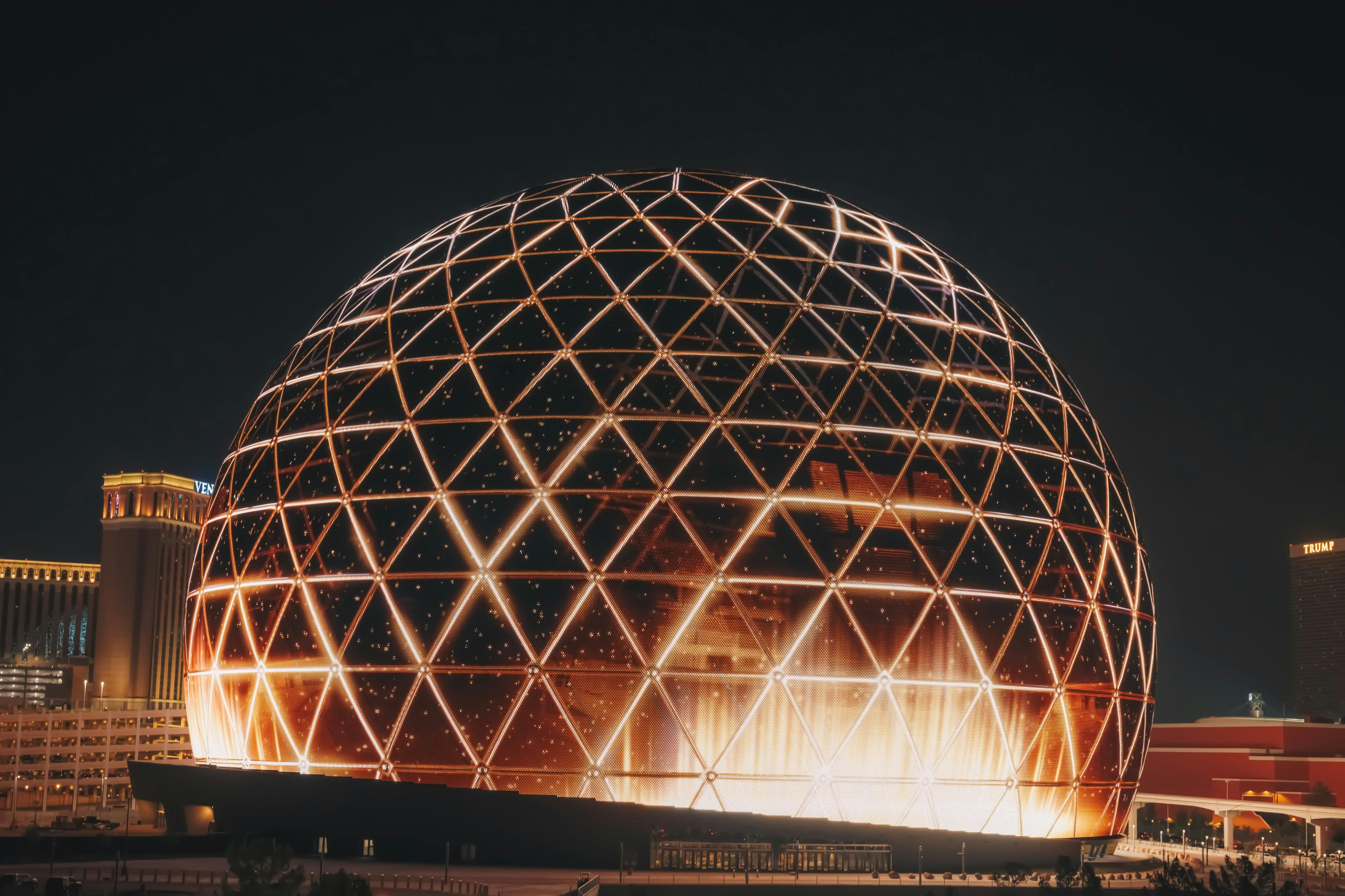 A large geodesic dome illuminated with warm lights against a dark night sky.