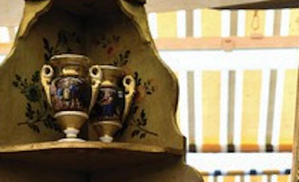 A table displays porcelain plates, vases, and figurines, with a framed portrait of a man in the background.