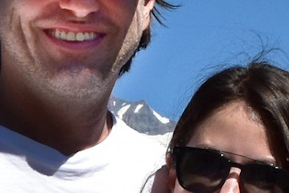 A couple poses together outdoors with a scenic mountain landscape and clear blue sky in the background.