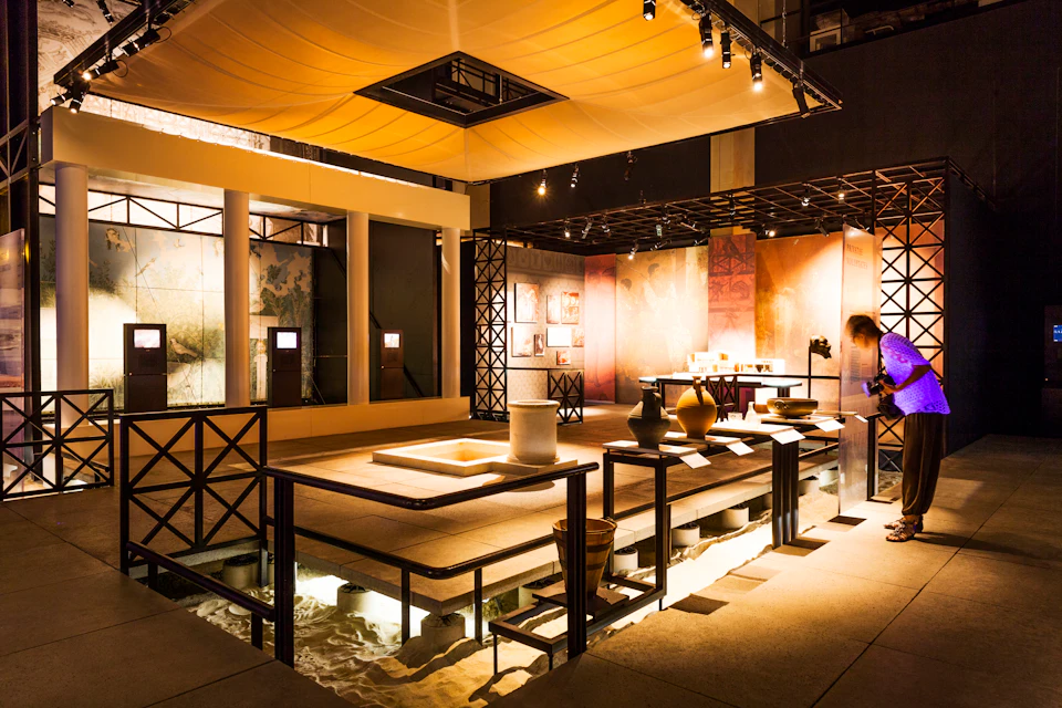 Exhibit featuring ancient pottery and artifacts displayed in a well-lit room with wooden railings and illuminated flooring.