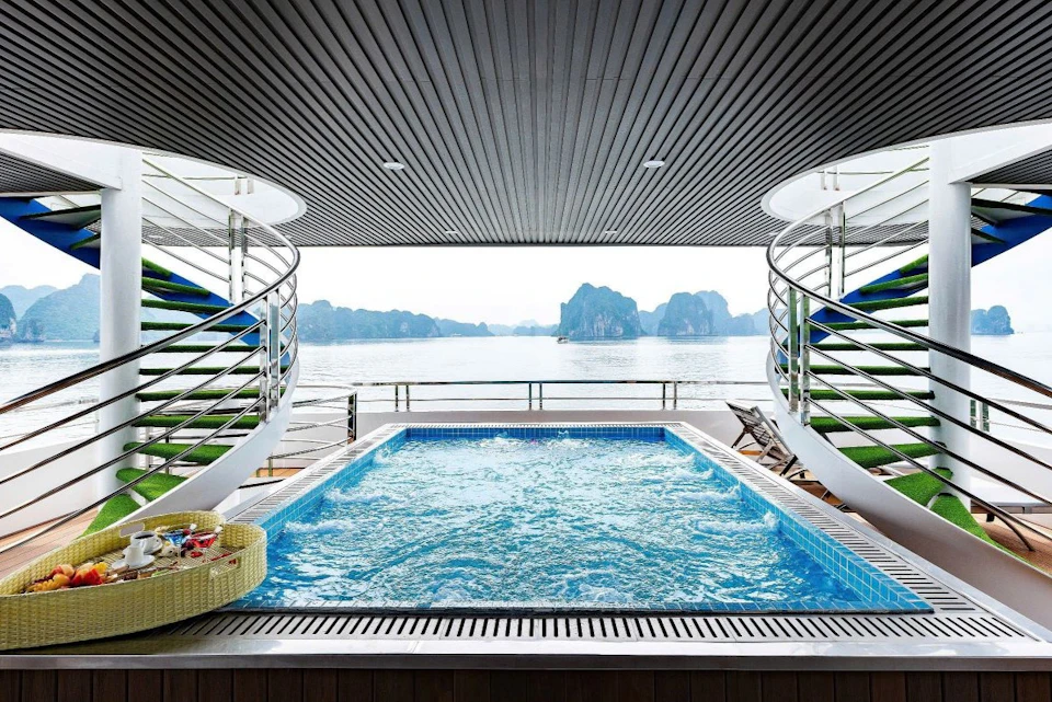 A rooftop pool on a boat with ocean views, surrounded by sleek railings, with a basket of towels and lounge chairs nearby.
