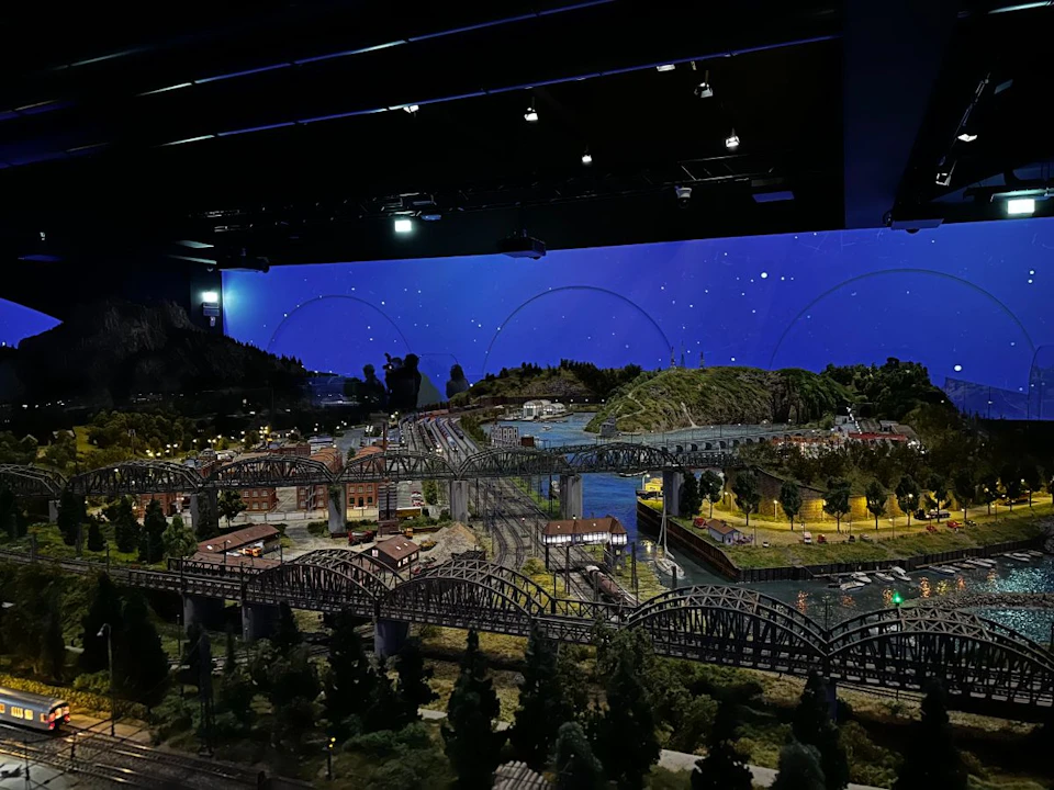 A detailed model railway layout with bridges, tracks, buildings, and trees, set against a backdrop of a starry night sky.