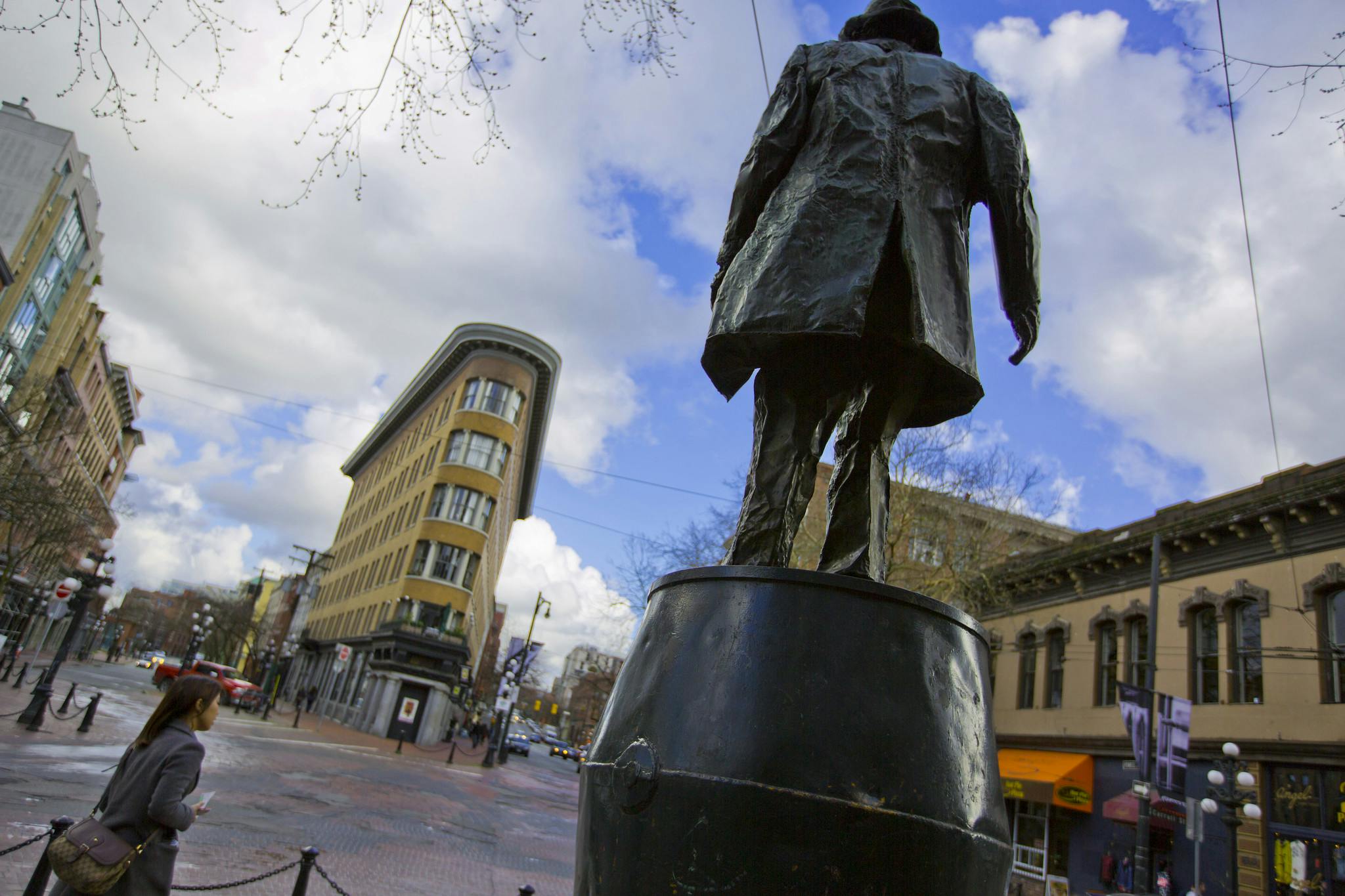 높고 좁은 건물을 배경으로 길거리 교차로가 내려다보이는 동상입니다. 한 사람이 근처를 걷고 있습니다.