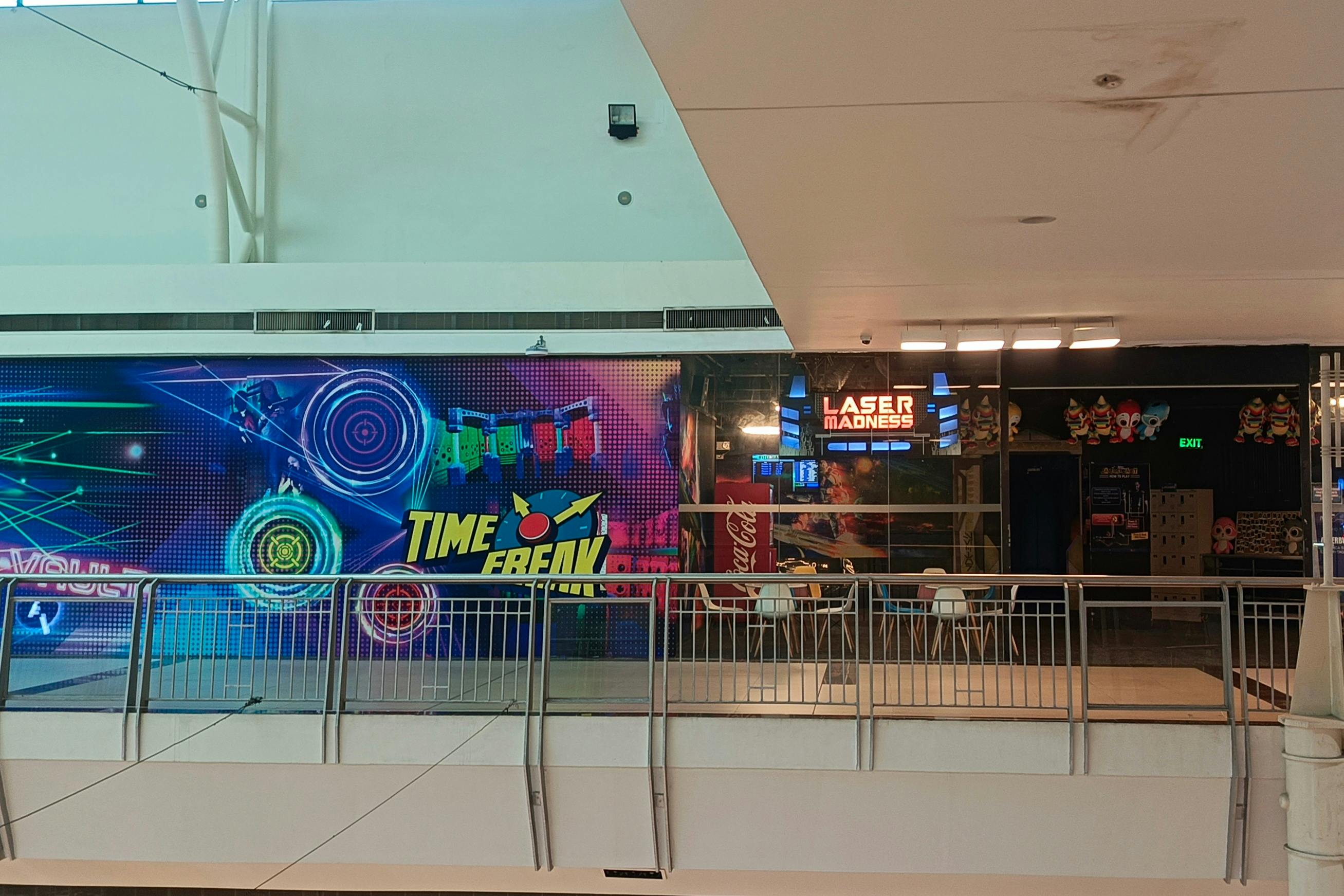 A mall interior featuring a laser tag venue called 'Laser Madness' and a colorful display with the text 'Time Freak.'