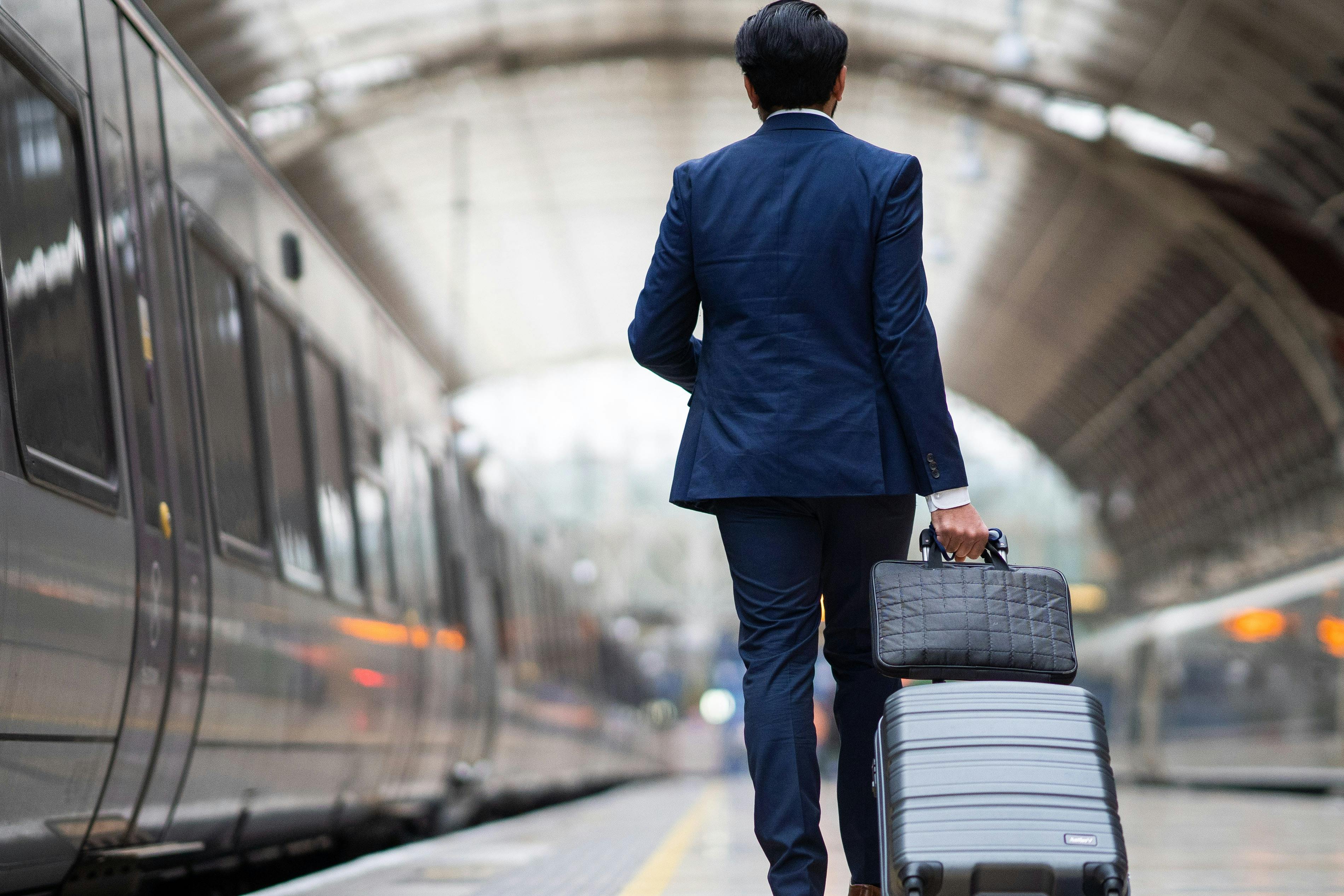 穿着西装的人在火车站台上行走，手提箱和包，两侧都可以看到火车。
