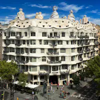 Um edifício grande e ornamentado, com paredes onduladas, numerosas janelas e chaminés curvas únicas no telhado, num cenário de céu azul.