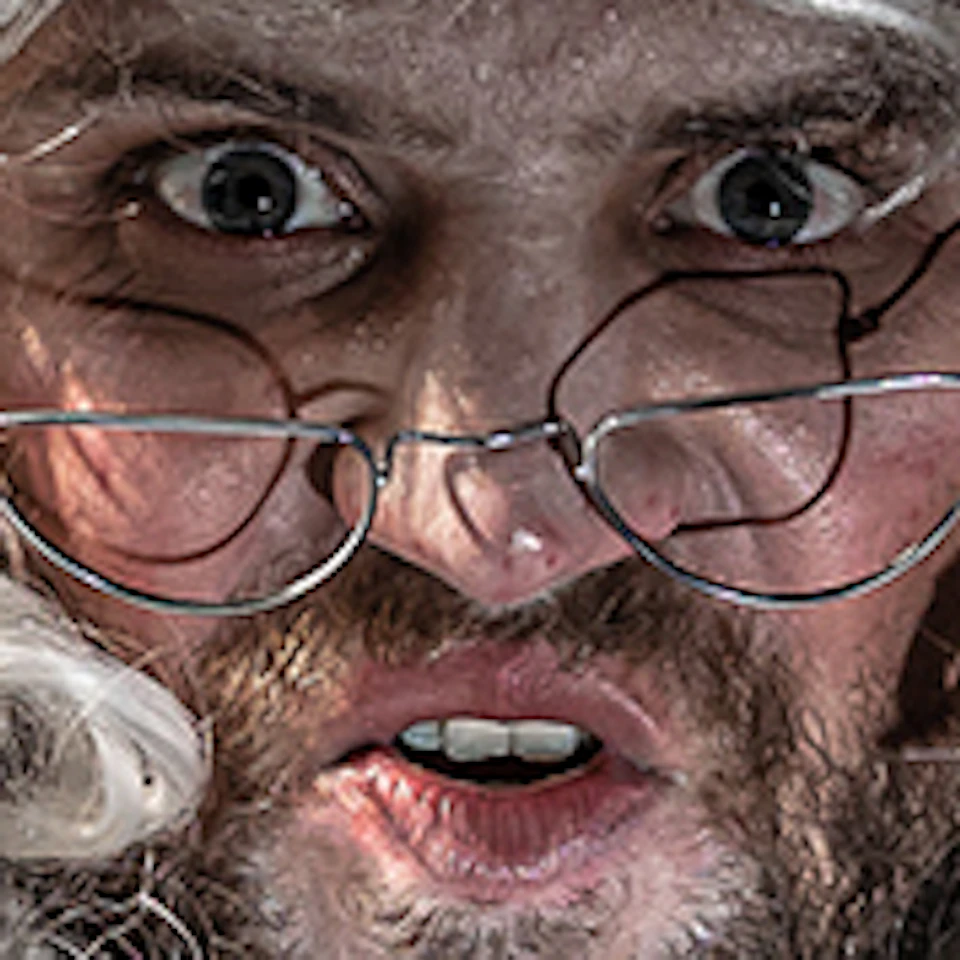 Man with curly white wig and glasses in period costume pointing finger while reading from a book in a vintage room.