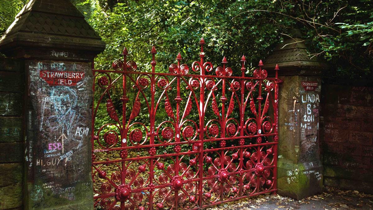 빽빽한 녹지로 둘러싸인 돌기둥 사이에 세워진 정교한 패턴의 화려한 붉은 연철 게이트.