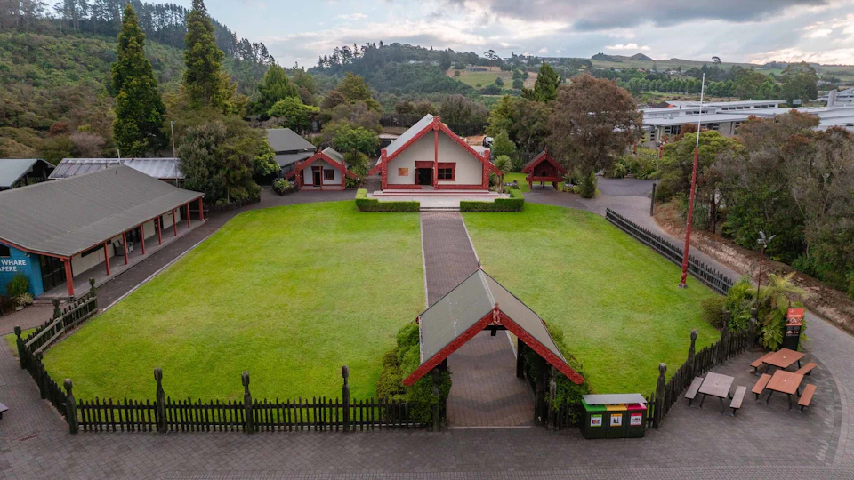 A traditional-style building with red accents and a triangular roof, surrounded by greenery and a pathway leading to it.