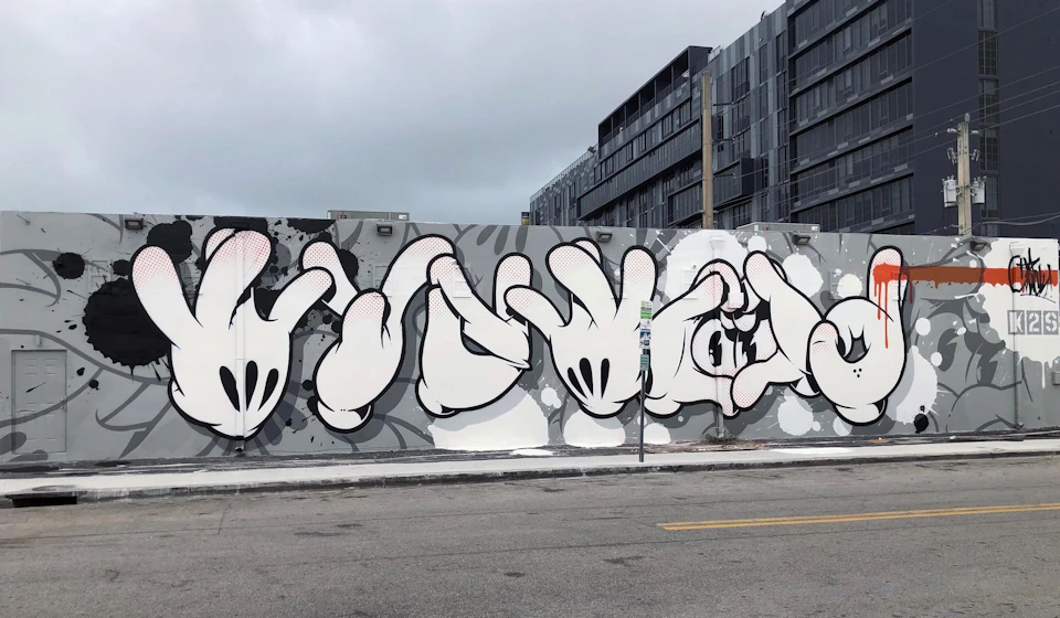 Graffiti on a wall depicting a series of stylized, cartoon-like hands in various positions, with a gray building in the background.