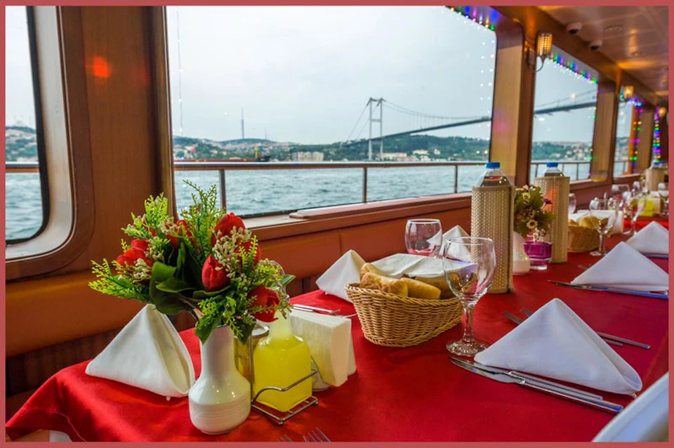 Table set with flowers, drinks, and bread, against a backdrop of a large bridge over water.