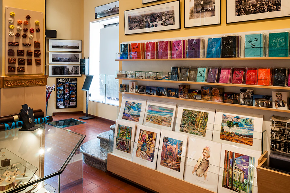 A museum gift shop with framed art on the walls, shelves with books, postcards, and art prints on display.