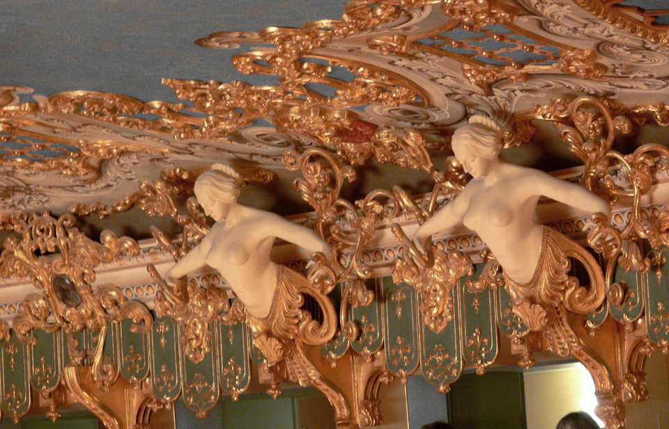 Ornate golden ceiling with sculpted female figures, intricate patterns, and green accents.