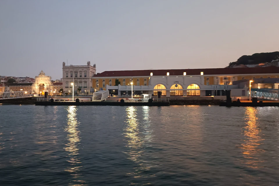 Buildings along a waterfront at dusk, with lights reflecting on the calm water.