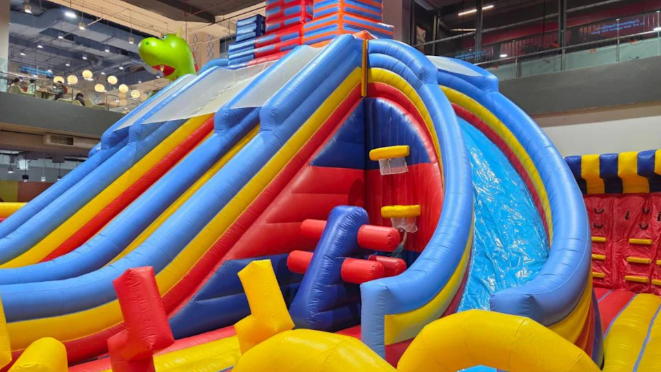 Colorful inflatable slide with blue, red, and yellow sections inside an indoor play area.