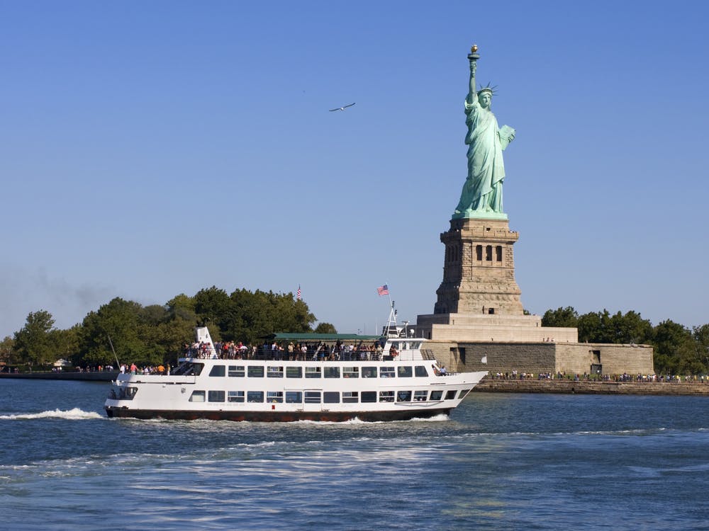 A passenger ferry moves across the water in front of the Statue of Liberty on a clear day.