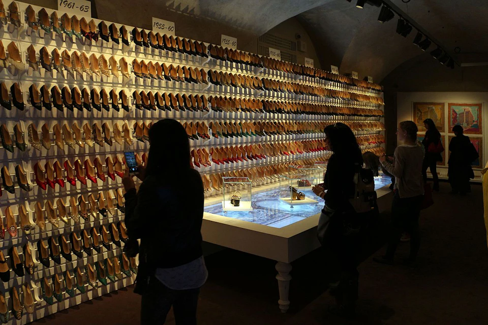 People browsing a display of numerous pairs of shoes organized in rows on a wall, with years labeled at the top.